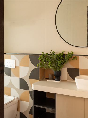 Bathroom vanity corner with round mirror, potted plant, and geometric mustard-charcoal tile wall
