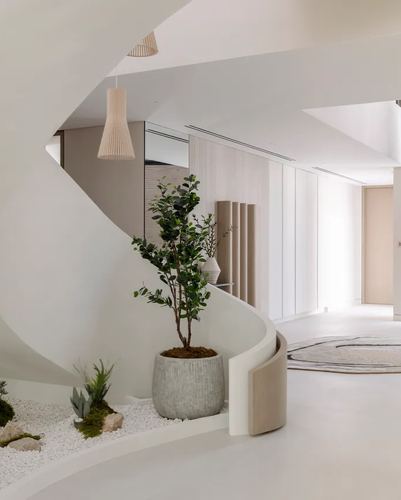 Curved white staircase with a pebble garden and potted tree in a minimalist Dubai villa foyer