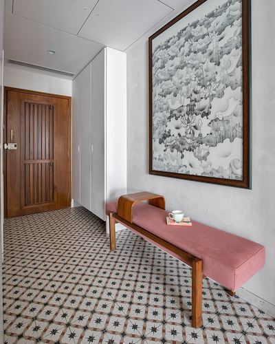 Entryway with patterned tile floor, wooden door, white wardrobe, framed artwork, and pink upholstered bench