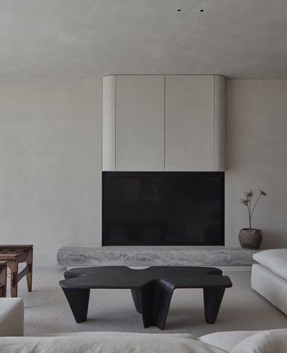 Minimalist living room with curved plaster cabinet, black sculptural coffee table, and stone hearth ledge
