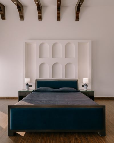 Bedroom with teal velvet bed centered under a plaster wall of arched niches and exposed ceiling beams