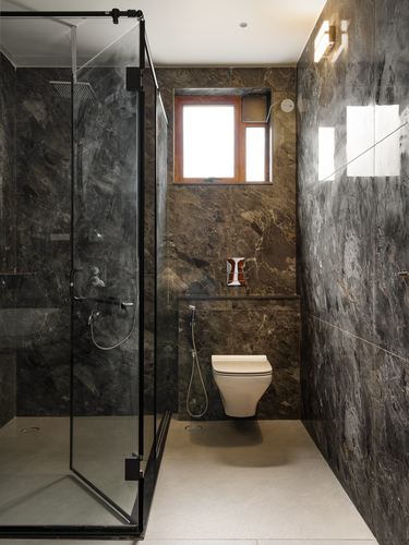 Dark stone-clad bathroom with glass shower, wall-hung toilet, and small window