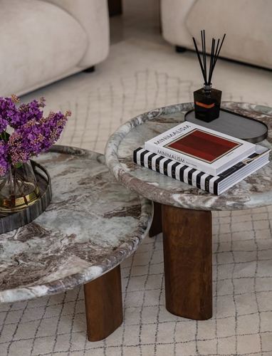 Two round marble coffee tables with wooden legs, styled with books, flowers, and a diffuser on a textured rug