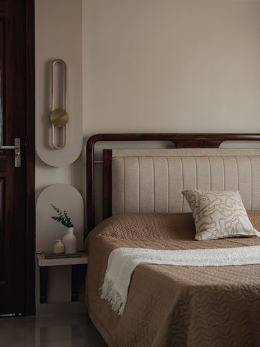 Bedroom corner with dark wood headboard, linen upholstery, brass sconce and arched floating nightstand