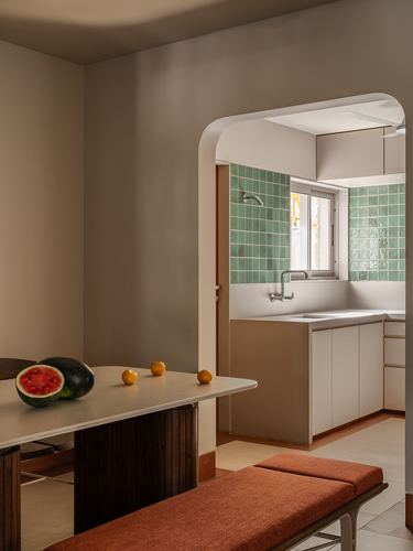 Dining table with fruit beside arched opening into a green-tiled kitchen, Surat home