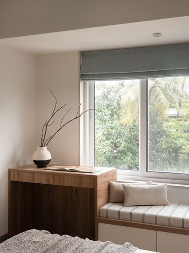 Window seat with striped cushions beside a wooden console holding a ceramic vase, greenery visible outside