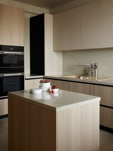 Minimalist kitchen with wood cabinetry, stone island, and built-in black ovens.