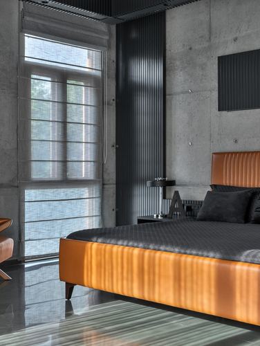 Bedroom with ribbed orange leather bed against raw concrete wall and sheer curtained window