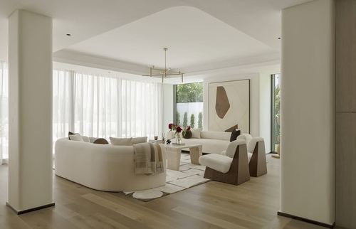 Curved white sofa and wedge-shaped armchairs in a sunlit neutral living room with wood flooring