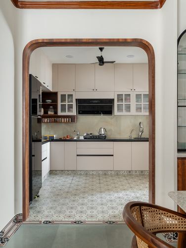 View through a curved wooden archway into a beige kitchen with patterned tile floor