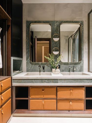 Double vanity bathroom with green marble backsplash, brass-framed mirrors, and tan leather drawer fronts