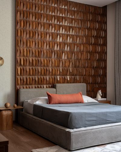 Bedroom with faceted wood geometric wall panel behind grey upholstered bed with orange bolster