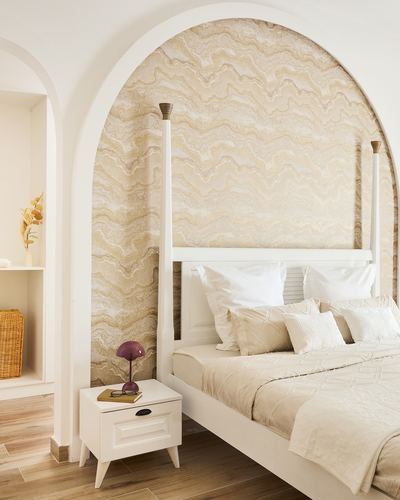 White four-poster bed set within an arched niche with a wavy beige patterned wallcovering.