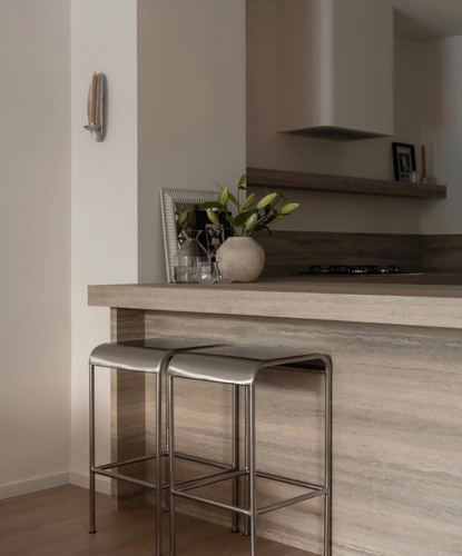 Minimalist kitchen island in stone with two metal stools and a vase of greenery