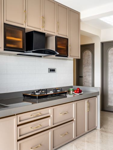 Beige kitchen with black chimney hood, reeded glass cabinets, grey stone countertop and gas hob.