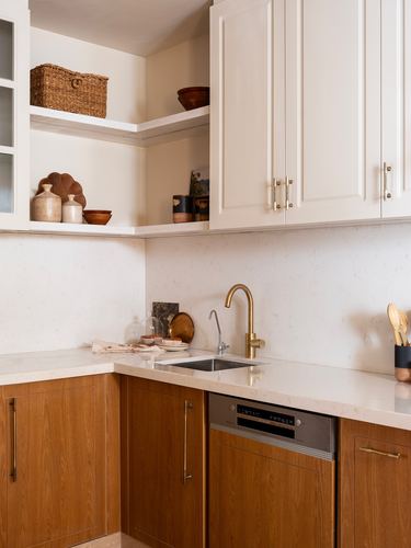 Corner kitchen with white cabinetry, wood-front lower units, brass tap, and open shelves with ceramics