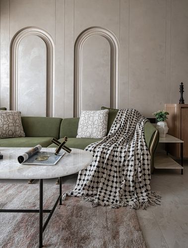 Olive sofa with patterned throw beneath two arched plaster wall niches and a round marble coffee table