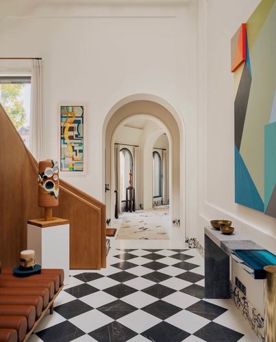 Foyer with black and white checkerboard floor, arched doorway, wooden staircase, and colorful artwork