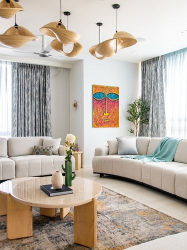 Curved beige sofas around a round marble coffee table beneath sculptural wood pendant lights