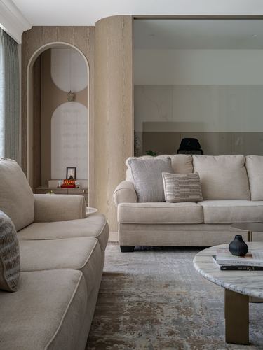 Beige living room with curved wood wall, arched niche, and two neutral sofas around a marble coffee table
