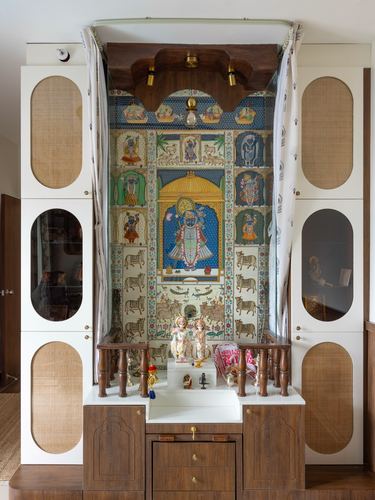 Pooja unit with cane-panelled cabinets flanking a wooden shrine painted with a pichwai mural and small deity idols