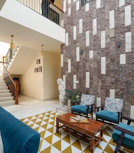 Double-height living space with textured stone wall, staircase, and teal armchairs on triangular tiled floor