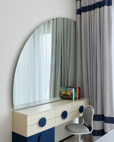 Arched mirror above a cream dresser with navy drawer pulls beside striped curtains and a grey chair