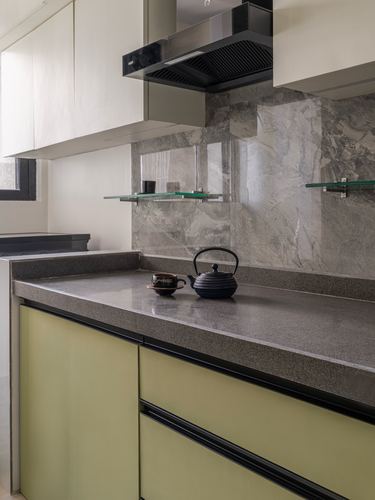 Corner of a modern kitchen with grey stone backsplash, black chimney hood, and olive cabinetry