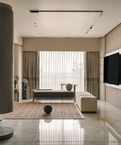 Minimalist beige living room with low bench, ottoman, spheres, sheer-curtained window and tv wall