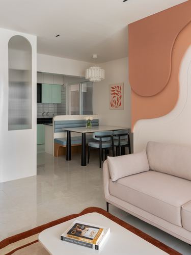 Living and dining area with curved terracotta wall, blue banquette, and beige sofa in Pune apartment