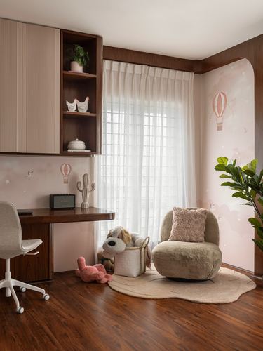 Child's study corner with wooden desk, sheer curtains, plush chair, and pink balloon wallpaper
