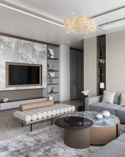 Living room with marble tv wall, camel bench, grey sofa and layered round coffee tables under a crystal chandelier