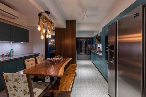 Long green kitchen with live-edge dining table, pendant lights, and stainless fridge at end