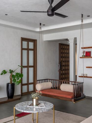 Suspended wooden swing daybed with rust cushions in a muted, textured living room in Rajkot