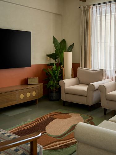 Living room with terracotta half-wall, wall-mounted tv, wooden console, plants and cream armchairs on a patterned rug