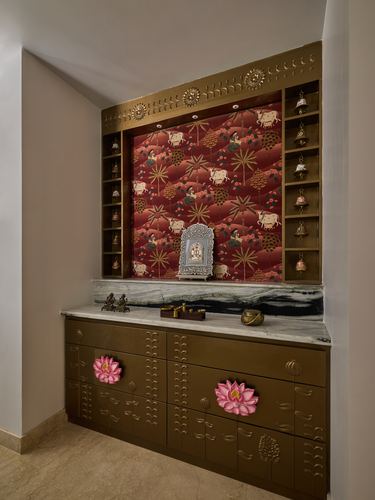 Pooja unit niche with brass shelving, hanging bells, red printed panel, and marble-topped bronze cabinet below