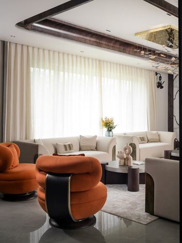 Living room with orange curved velvet chairs, cream sofas, sheer curtains and a beamed ceiling