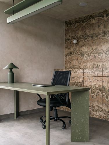 Olive terrazzo desk with black mesh chair against a wavy stone-patterned accent wall.