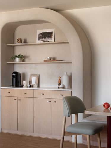 Arched plaster niche with wood cabinetry and shelving beside a dining table with sage chair