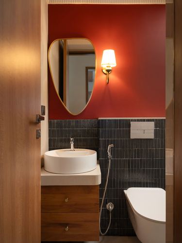 Bathroom with red wall, ribbed dark tile, wooden vanity with vessel sink and brass sconce lighting