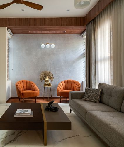 Living room with orange scalloped chairs, grey textured wall, brass Buddha statue and marble floor