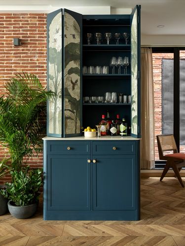 Teal built-in bar cabinet with botanical-lined doors open against exposed brick wall