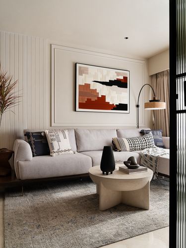 Neutral living room with panelled wall, abstract art, cane-shaded arc lamp and stone coffee table