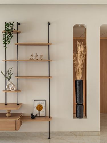 Wall-mounted wood shelving beside an arched niche holding tall black vases with dried grass