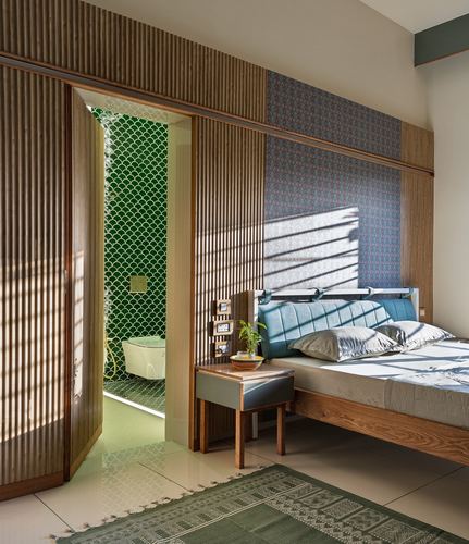 Bedroom with fluted wood paneling, striped light, and view into a green tiled bathroom