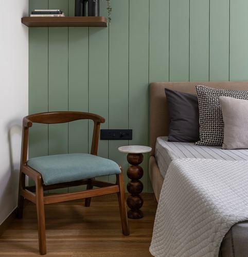 Bedroom corner with wooden armchair, bobbin side table, and bed against green paneled wall