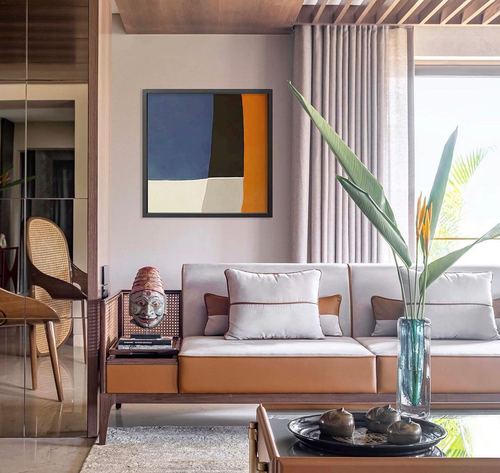 Living room with tan leather sofa, cane console, mask sculpture, abstract art and tropical leaves in glass vase
