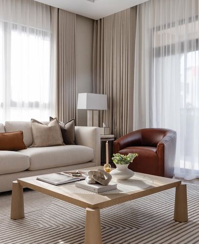 Neutral living room with beige sofa, leather swivel chair, wood coffee table, and sheer curtains