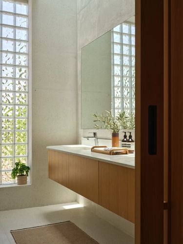 Floating wood vanity with mirror beneath a tall glass block window in a minimalist bathroom