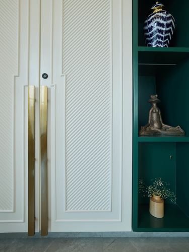 Fluted white wardrobe with long brass handles beside a dark green shelving niche with decor objects